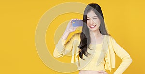 Cheerful asian woman showing credit card mockup standing with copy space over isolated yellow background. Smile Asian girl