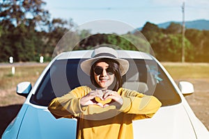 Cheerful asian woman showing hand heart shape while standing with new car on road,Happy and smiling,Car insurance concept