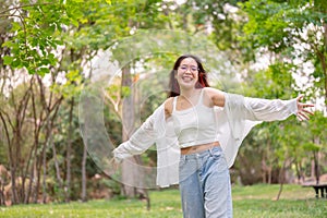 A cheerful Asian woman smiles warmly while spinning around in a park, showing a joyful expression