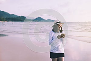 Cheerful asian woman using cell phone on the beach near sea while beautiful sunset time,Happy and smiling,Relaxing and enjoying co