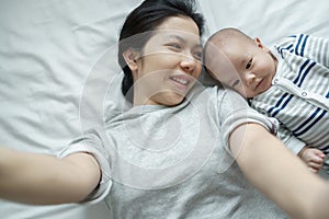 Cheerful Asian Young mother and son taking selfie with mobile phone on bed. Loving Family