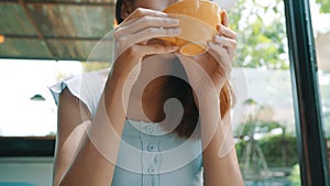 Cheerful asian young woman drinking warm coffee or tea enjoying it while sitting in cafe.