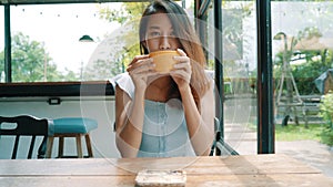 Cheerful asian young woman drinking warm coffee or tea enjoying it while sitting in cafe.