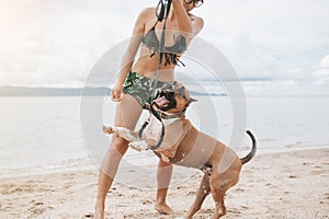 Cheerful asian young woman in eyeglases playing with her dog on the beach