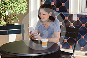 Cheerful asian young woman sitting in cafe drinking coffee and using smartphone for talking, reading and texting.