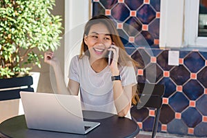 Cheerful asian young woman sitting in cafe drinking coffee and using smartphone for talking, reading and texting.