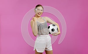 Cheerful Asian Young woman in white t-shirt over isolated pink background looking at camera and holding a soccer ball