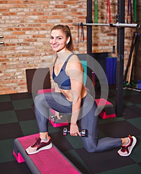 Cheerful athlete woman doing lunges with dumbbells