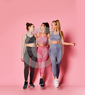 Cheerful athletic girls friends in pink, grey, brown training suits walk together chatting. Fitness and yoga girls