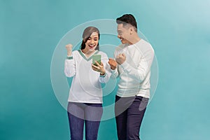 Cheerful attractive couple standing isolated over blue, using mobile phone, celebrating success