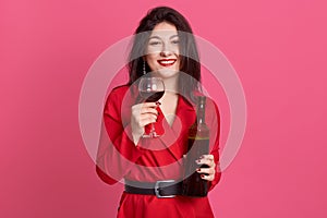 Cheerful attractive darkhaired young woman with bright makeup, holding bottle of wine and glass, lady with toothy smile