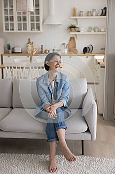 Cheerful attractive mature woman sitting on soft couch at home