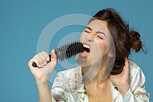 Cheerful attractive teen girl sing song holding comb like a microphone in the morning, over blue