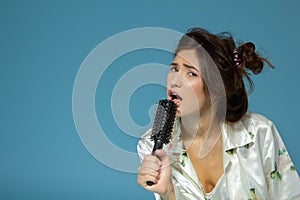 Cheerful attractive teen girl sing song holding comb like a microphone in the morning, over blue