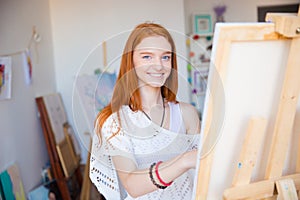 Cheerful attractive woman artist painting on canvas in art workshop