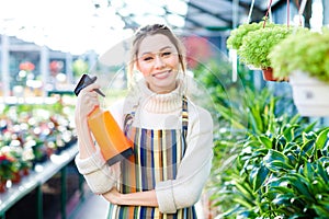 Cheerful attractive woman gardener standing in orangery with water pulverizer