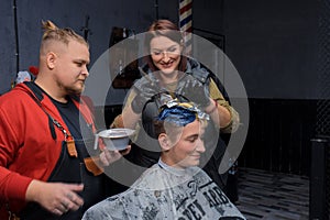 Cheerful attractive woman professional European hairdresser with a man next to her in the process of dyeing hair in color to a
