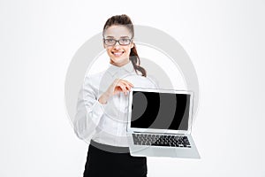 Cheerful attractive young businesswoman in glasses holding blank screen laptop