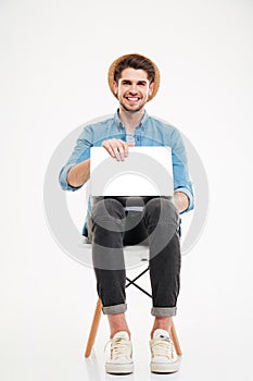 Cheerful attractive young man in hat sitting and using laptop