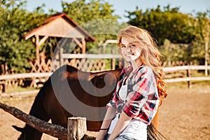 Cheerful attractive young woman cowgirl with horse in village