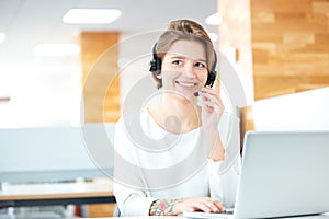 Cheerful attractive young woman working with headset and laptop