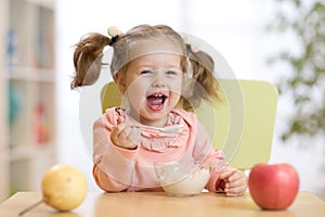 Cheerful baby child eating food itself with a spoon