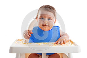 Cheerful baby child eats food itself with hands. Portrait of happy dirty kid boy in high chair and mess around