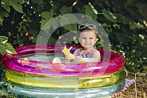 Cheerful baby enjoying her day in sumer in her pool holding plastic scoop