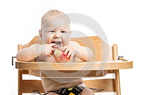 Cheerful baby girl eating apple while sitting in high chair