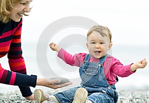 Cheerful baby girl and her mother playing on the beach