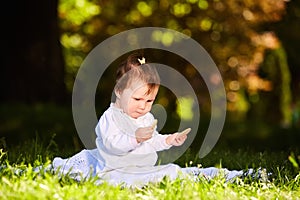 Cheerful baby girl sitting on the green grass in the city park at summer day.