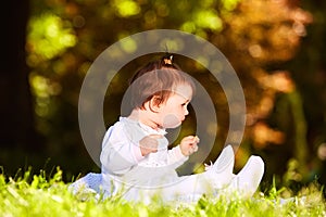 Cheerful baby girl sitting on the green grass in the city park at summer day.