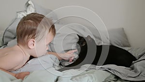 Cheerful baby playing with black cat in parents bed.
