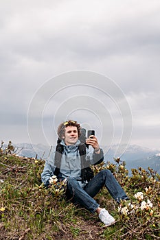 Cheerful backpacker is shootting the video while sitting on the hill