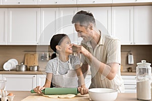 Cheerful baker father touching face of daughter with floury finger