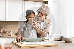 Cheerful baker grandma touching nose of grandkid with floury finger