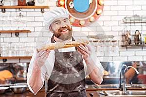 Cheerful baker showing loaf of bread on the kitchen