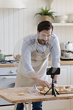 Cheerful baking blogger man in apron recording preparation of bakery