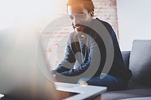 Cheerful bearded African man working on laptop while sitting sofa at his modern office place.Concept of young people