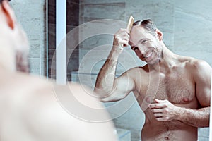 Cheerful bearded blonde-haired man smiling while looking into mirror