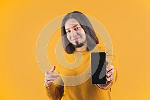 Cheerful bearded caucasian man showing his smartphone with blank screen. Technology concept. Studio shot over orange