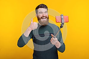 Cheerful bearded man makes a selfie whil showing thumb up and smiling .