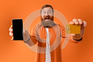 Cheerful bearded man showing cellphone screen and credit card, studio