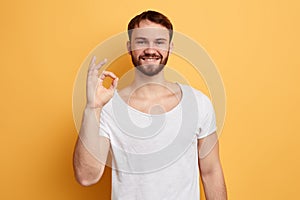 Cheerful bearded man showing okay gesture isolated on the yellow background