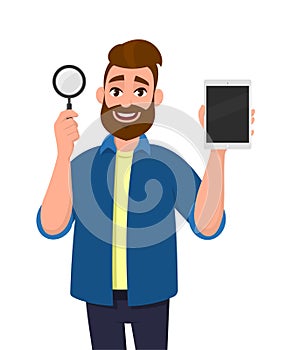 Cheerful bearded young man showing/holding magnifying glass and empty/blank screen tablet computer PC in hand. Search, find.