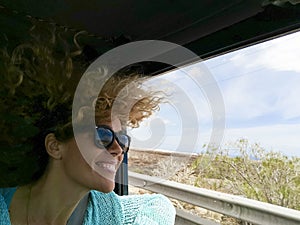 Cheerful and beautiful adult young woman enjoy the trip inside a car with open windows and wind in the hair - concept of happy