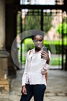 Cheerful beautiful afro american female making selfie on front camera of telephone for publishing in social networks outdoors in c