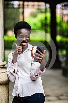 Cheerful beautiful afro american female making selfie phone with thumbs up for publishing in social networks outdoors in campus