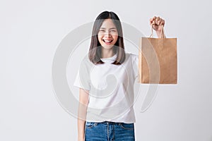 Cheerful beautiful Asian woman in a white t-shirt and holding brown blank craft paper bag.