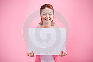 Cheerful beautiful asian young woman holding blank board on pink background